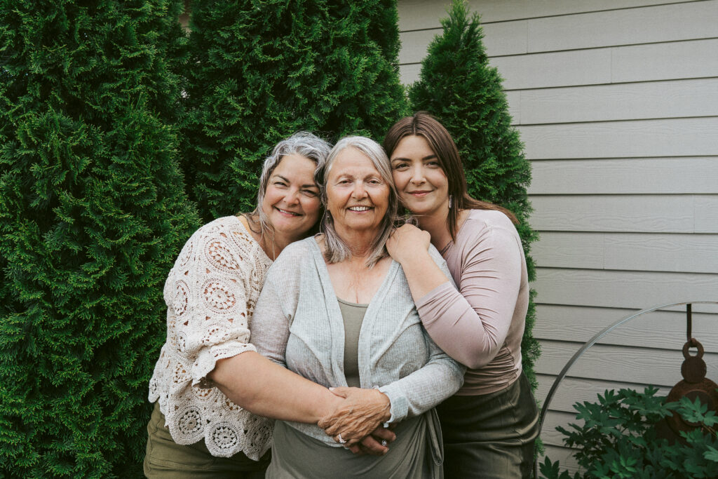 Mother, daughter and granddaughter smile in front of the camera for their photo session as an extended family.